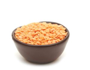 Orange lentils in a round brown cup isolated on a white background