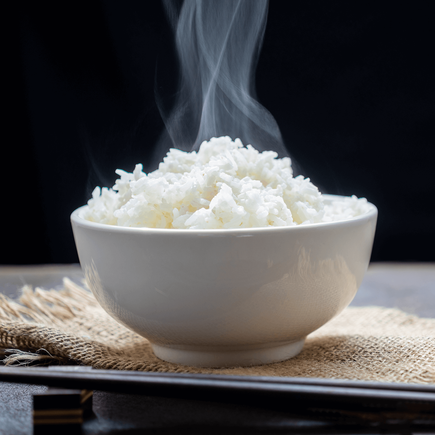 Cooked rice with steam in a black bowl on a dark background