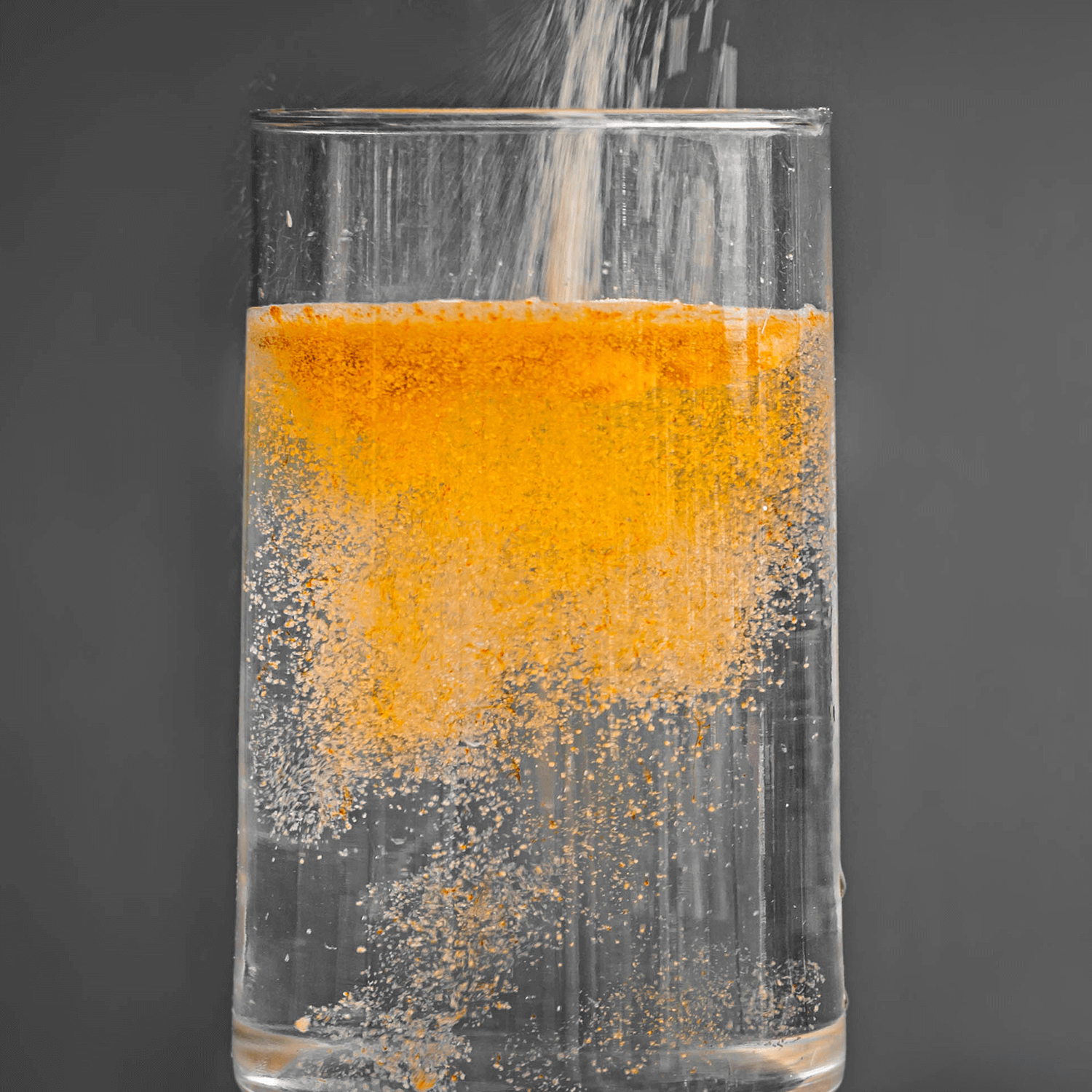 Action shot of an orange powdered drink mix being poured into a clear glass of water