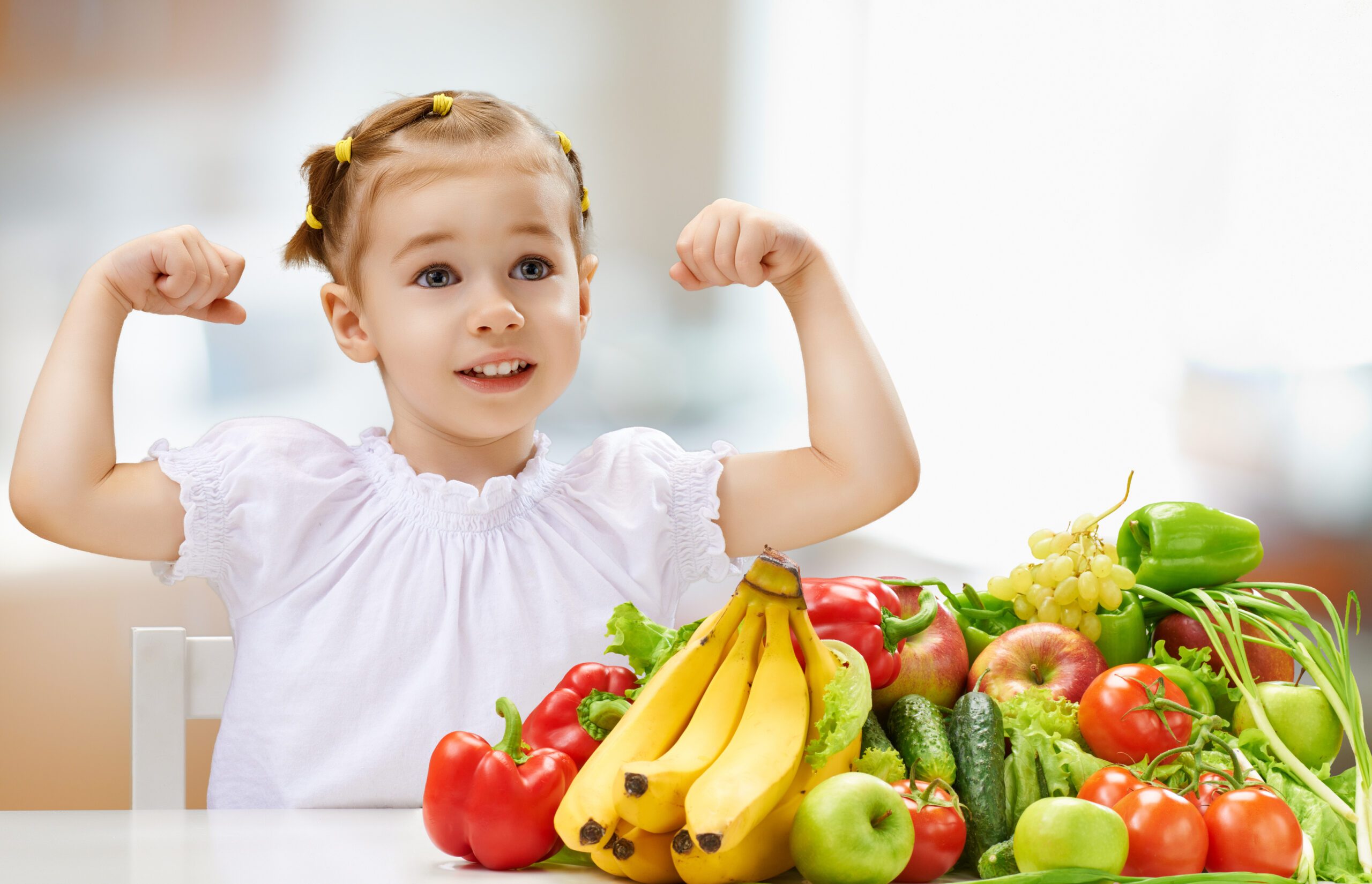 Little girl cheering next to a pile of fresh fruit