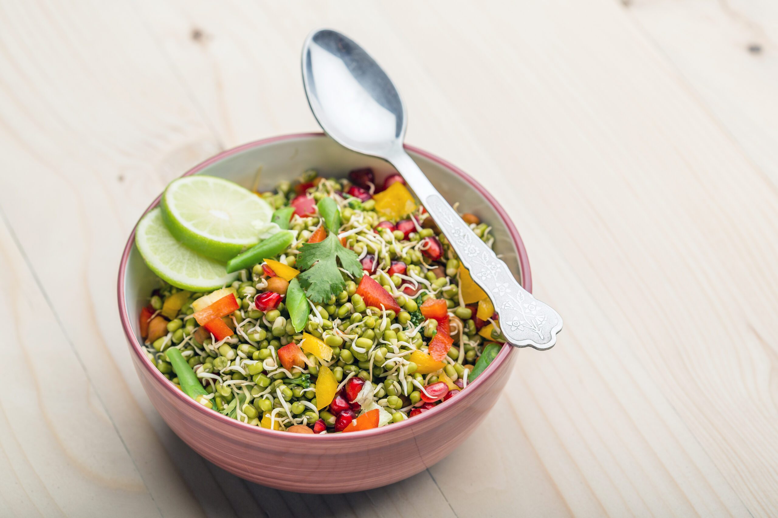 Sprouted lentil salad served in a white bowl with a silver spoon lying across the top