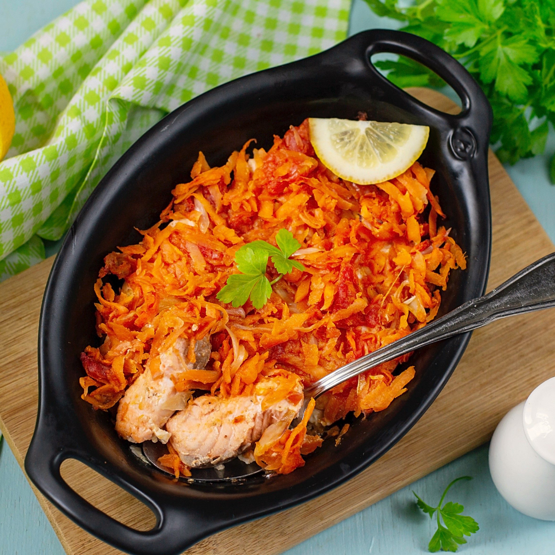 Cast iron pan filled with fish topped with grated carrots and a slice of lemon