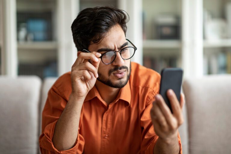 Confused middle eastern young man feel shocked, receive bad unexpected message on cellphone, frustrated guy disappointed by problems with business touching glasses, reading news, closeup, copy space