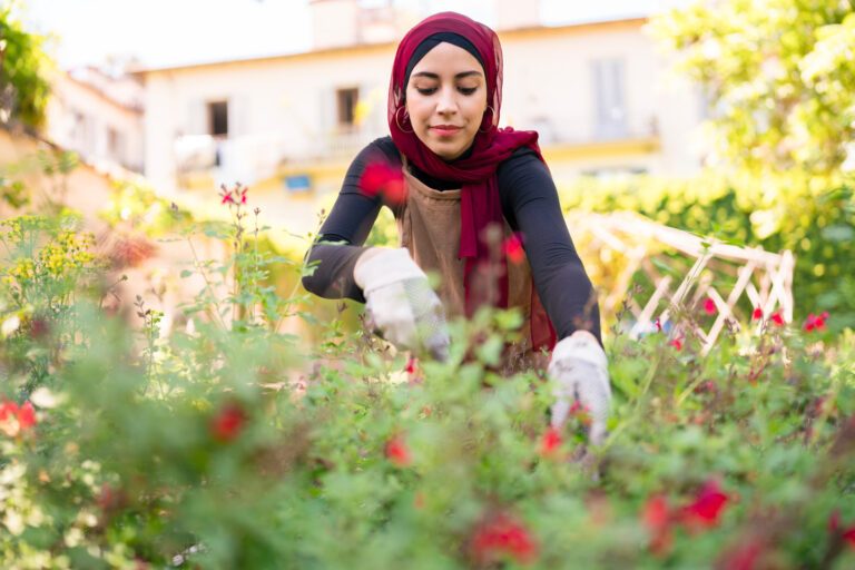 Low angle of content female gardener in gloves cultivating blooming flowers in urban summer garden
