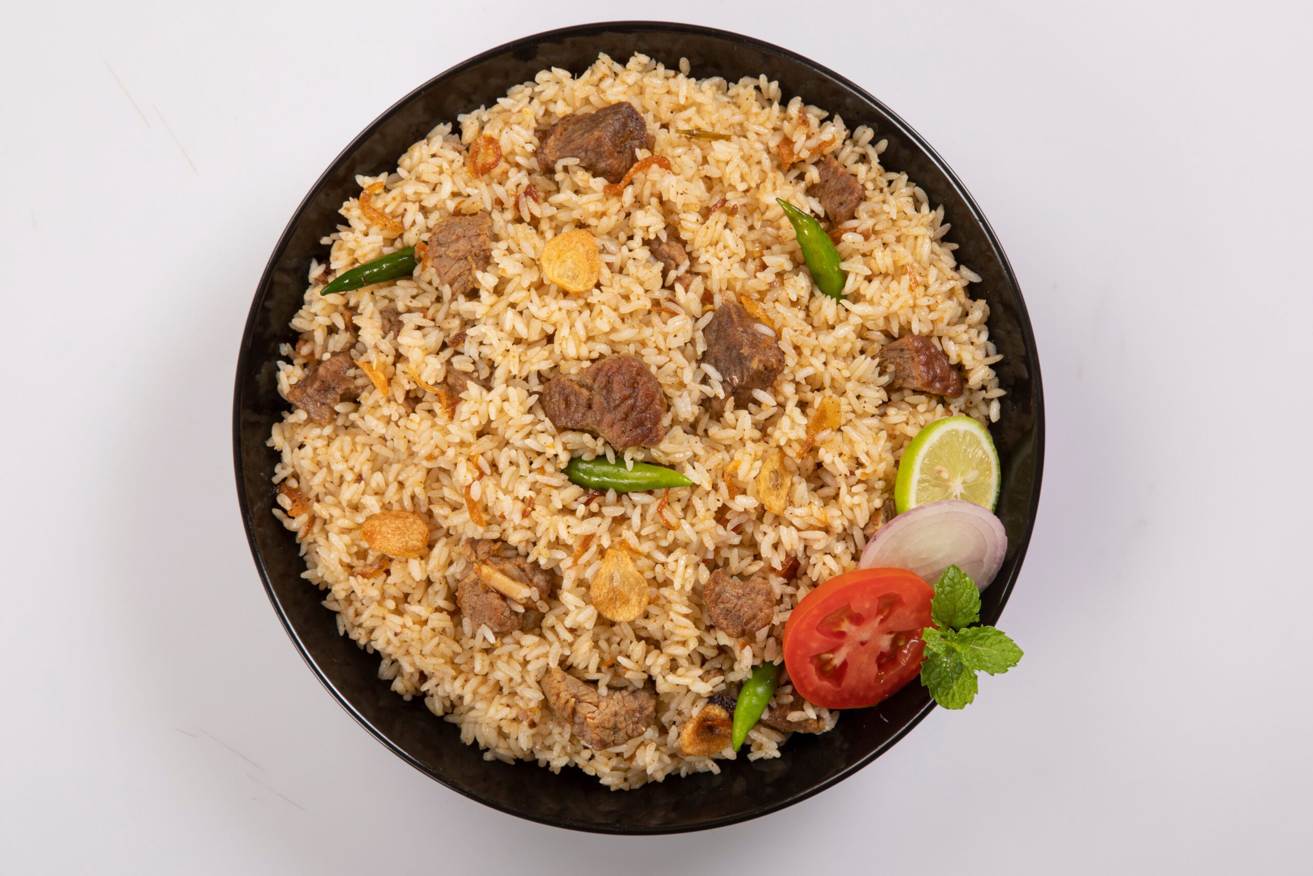 Yakhni pulao garnished with tomatoes, onions, lime, and green chilies