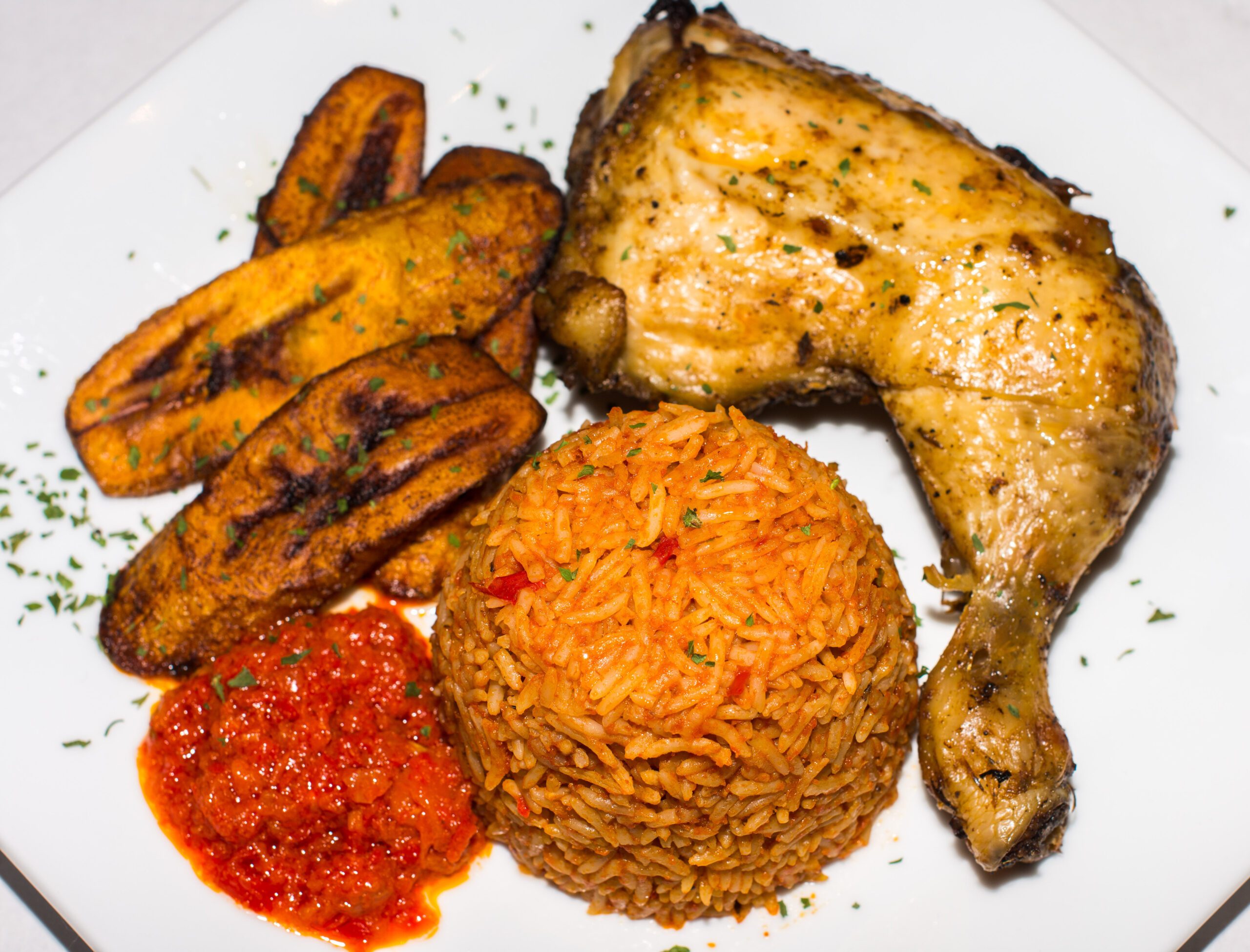 Nigerian Jollof served with Plantain, Chicken and spicy sauce