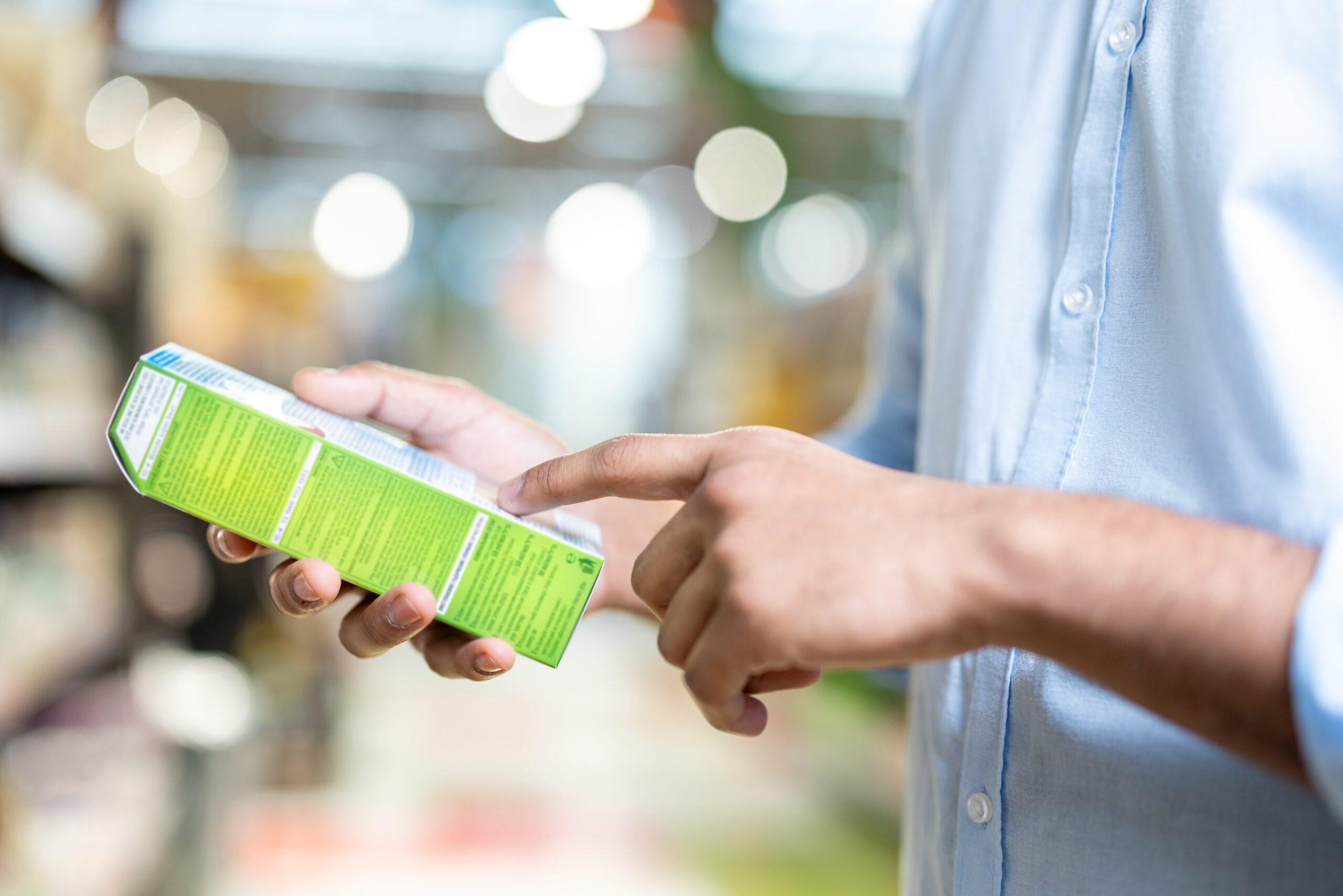 A man in a blue shirt is holding a green box and pointing at the details printed on it while shopping.
