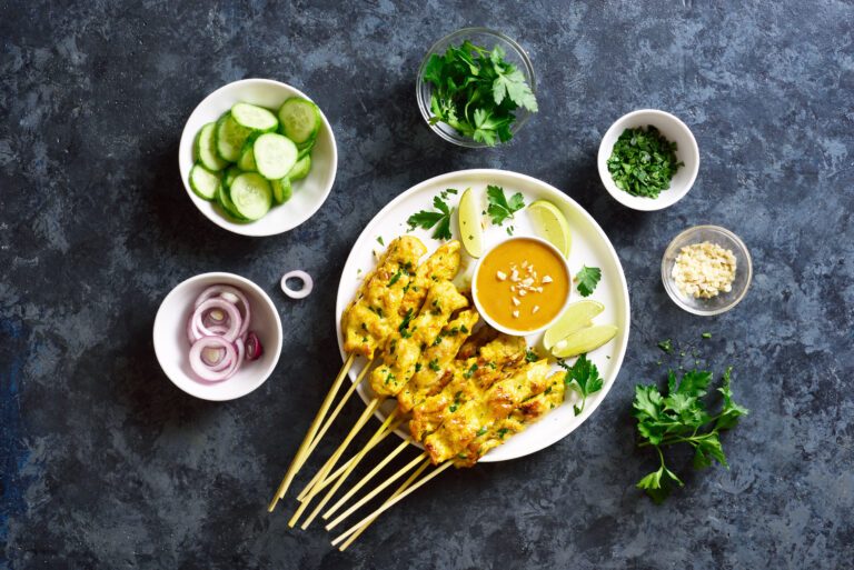 Chicken satay with peanut sauce. Grilled chicken skewers served with peanut dipping sauce. Tasty meal for dinner or party appetizers. Blue stone background, top view, flat lay