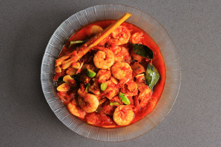 Chili prawns or Sambal Udang with petai or pete or mlanding (Parkia speciosa) cooked with mashed red chili and tomato in clear plate, with black background, top view.  Indonesia cuisine food.