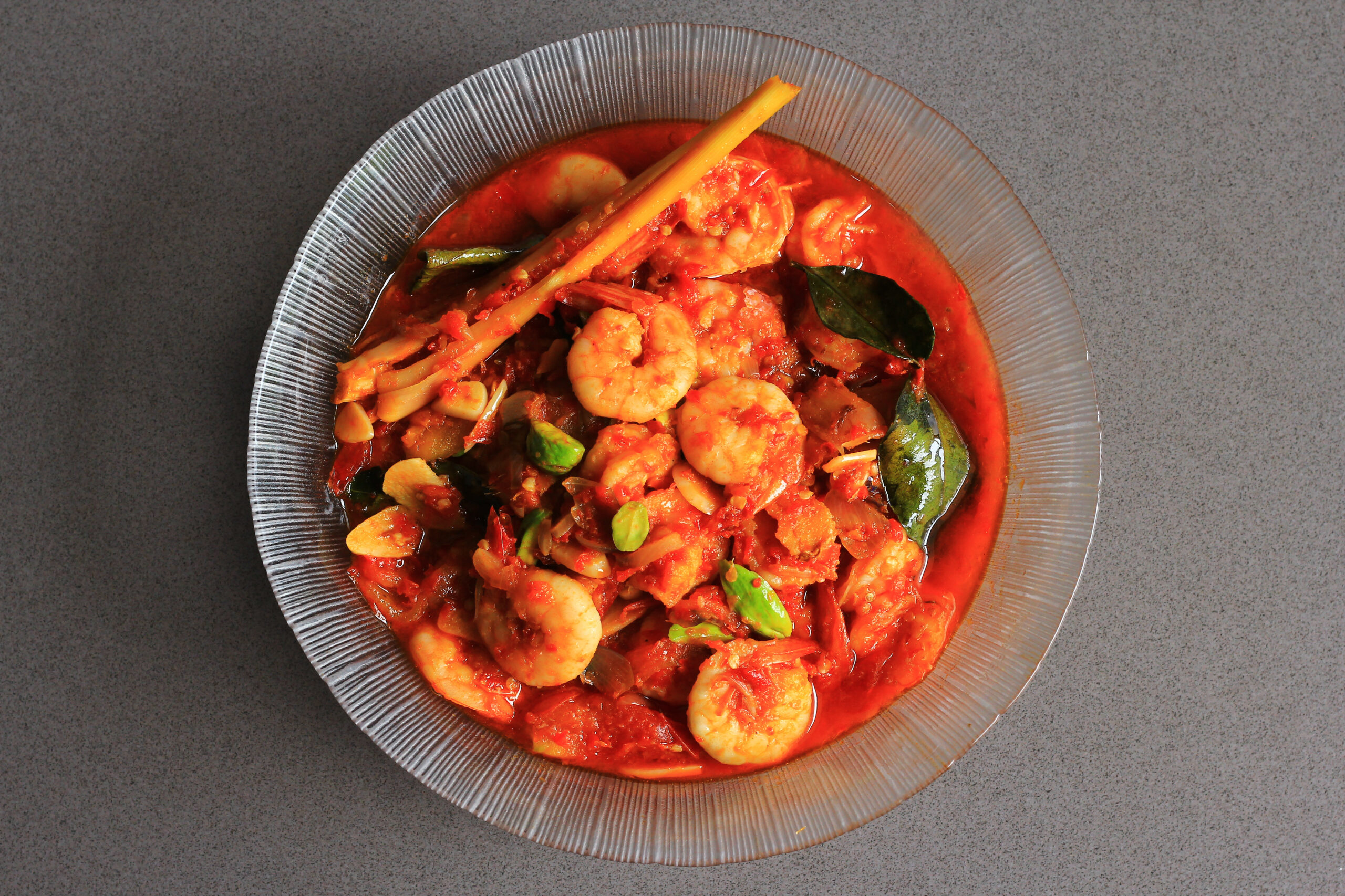 Chili prawns or Sambal Udang with petai or pete or mlanding (Parkia speciosa) cooked with mashed red chili and tomato in clear plate, with black background, top view.  Indonesia cuisine food.